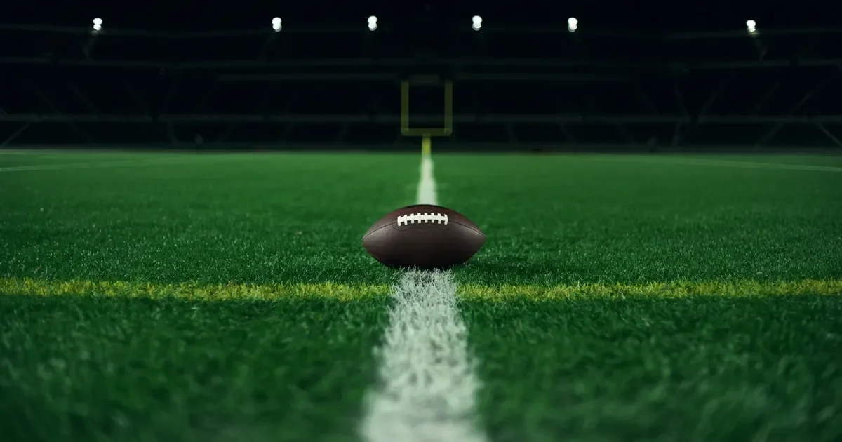 An American football on the goal line under stadium floodlights at night